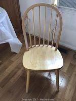 Single wooden chair showing front view with rounded seat and vertical slatted backrest, light natural wood finish, on hardwood floor.