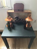 Wooden end table with two orange lanterns, carved wooden dragon, two glass jars, dark wooden box, and wooden napkin holder on top