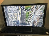 Front view of Sony 55" TV powered on, showing display and stand.