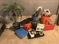 Overall view of lot items grouped together on basement floor showing the faux palm tree next to orange buckets, seed trays, soil testing equipment and packaging boxes.
