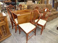 Six wooden dining chairs arranged near a wooden table, showing chair backs and upholstered seats.
