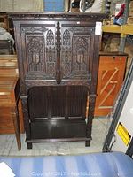 Front view of dark stained wooden cabinet with carved panels and open bottom shelf