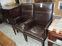 Front view of both chairs showing leather upholstery, wooden legs, and nailhead trim