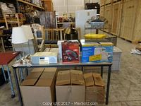 Wide view of table with all lot items including two lamps, boxed humidifiers, iLuv docking station, and boxes below