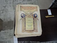 Stack of antique magazines showing 'National Monthly' cover with illustrated portraits and early 1900s decorative border.