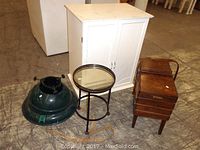 Lot items arranged including white cabinet, round glass top table, green metal Christmas tree stand, and sewing box.