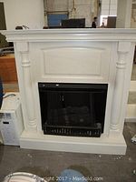 Full view of white corner fireplace with black metal insert and classical column details.