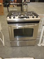Front view of stainless steel GE electric range showing oven door with glass window, handle, and control panel with knobs and buttons.