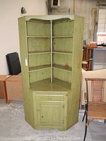 Front-side view of vintage green wooden corner cabinet showing shelving and general wear.