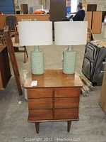 Front view of the nightstand with two ceramic lamps on top, showing wood grain and drawer details.