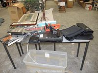 Overview photo showing a table with DVDs, electric chainsaw, griddler, and some soft DVD cases
