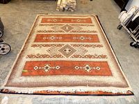 Full view of the southwestern design rug laid out flat on floor with geometric and diamond patterns in earthy rust and cream colors.