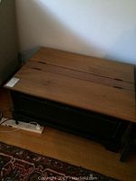 Full view of the wood coffee table showing light wood finish top with two distinct hinge lines and dark stained storage base underneath on hardwood floor.