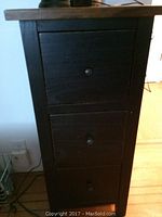 Front view of the dark stained three drawer stand with visible drawer knobs.