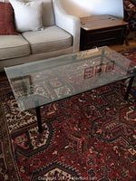 Rectangular glass coffee table with clear tempered glass top and black metal frame pictured in living room setting on red patterned rug.