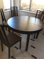 Full view of round dark wood table with four black chairs around it.