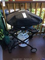 Front view of the Weber portable BBQ covered with black protective cover, showing the grill mounted on a portable wheeled stand with propane tank underneath.