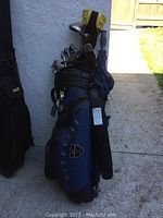 Nike golf carry bag filled with clubs and umbrella leaning against exterior wall