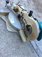 View of the entire Makita sliding compound mitre saw showing metal base, saw blade, and handle.