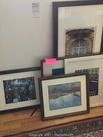 Framed art pieces collection leaning against a wall, including landscape painting, architectural print, and photo of KD Lang.