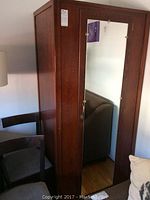 Front view of wooden wardrobe with full-length mirror on the door, showing overall design and condition including lock area without key.