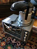 Side view of the Omega Juicer BMJ330 placed on top of the KitchenAid countertop oven KCO223CU with visible power cords and dark top juicer dome.