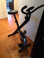 Side view of black and silver foldable exercise bike with padded seat and handlebars.