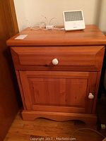 Closed view of solid wood night stand with white knobs, power cords visible behind and Philips SAD lamp on top.