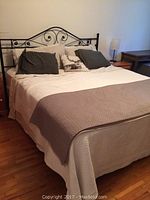 Full view of king size bed with black metal frame and bedding showing decorative scrollwork on headboard.