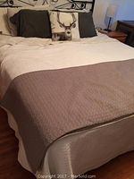 Full view of a made bed showing a beige quilted bed cover, cream underneath, and pillows including one with a deer print.
