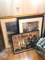 Large gold framed print of ocean and bridge alongside a black framed black and white photo and a U.S. Route 66 framed sign with 3D motorcycle.