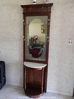 Full view of the wood entry way coat table with large mirror, hooks, marble top, and lower shelf.
