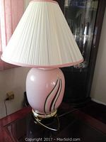 Full view of one lamp showing pink glass base with wavy black and white design and pleated cream shade with pink trim.