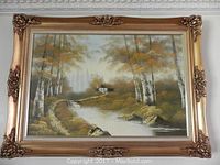 Full view of framed artwork showing a stream, wooded landscape with a cabin, surrounded by ornate gold frame.