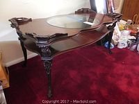 Full view of the wood coffee table showing circular glass inset, carved sides, and curved legs.