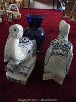 Pair of white ceramic elephant bookends and cobalt blue glass vase on red carpet