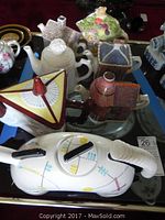 Photo of seven collectible tea pots, some shaped like houses with decorative motifs, and one modern abstract white tea pot.