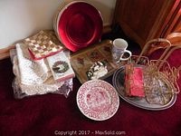 Photo showing various Christmas-themed dishes, gold wire baskets, lace linens, napkins, and kitchen textiles arranged on the floor.