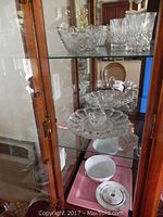 Wood cabinet with shelves holding cut crystal bowls, cups, and dishes along with some white ceramic pieces