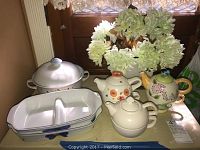 Photo showing all items in the lot including teapots, serving platters, lidded dish, and faux flowers arranged on a table