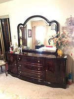 Full front view of cherry veneer dresser with three drawers, side cabinets, brass ring pulls, and attached matching mirror with scalloped top