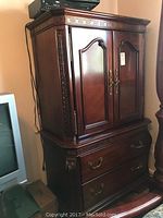 Photo of entire armoire from an angle showing top section with closed double doors, carved trim, and two large bottom drawers with brass handles.