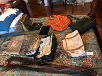Image of assorted handbags, wallets, and belts laid on bedding, showing variety of styles and materials