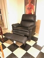 View of black recliner with footrest extended, showing padding on armrests and backrest.