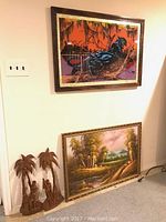 View of four artwork pieces: the panther wall art mounted on wall, a forest-themed framed painting leaning against the wall, and two carved wooden sculptures positioned on the floor.