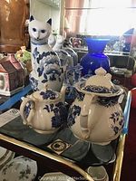 View of the three blue and white ceramic teapots and the ceramic cat figurine on a shelf.