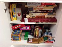 Photo showing a wider view of the games with visible titles including Mad Gab, Whatzit?, Taboo, and Boggle Jr. among others, stored in a cupboard shelf.