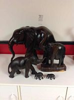 Overview photo of six elephant carvings in ebony and mahogany woods placed on white surface.