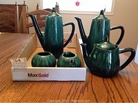 Full set of Blue Mountain Pottery on wooden table including two tall coffee pots, one shorter tea pot, and sugar and creamer in a box.