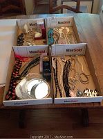 Full view of the jewelry lot with multiple cardboard trays containing various jewelry pieces including belts, necklaces, bracelets, earrings, cuff links, and other accessories displayed on a wooden table.